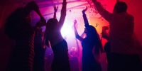 A crowd of people in silhouette raises their hands against colorful neon light on party background